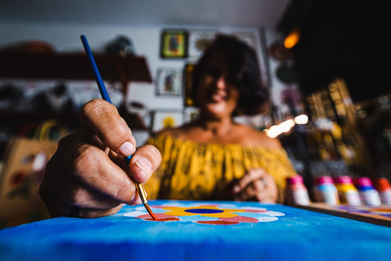 Mulher pintando tela com foco na mão dela com o pincel.