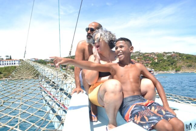 Imagem de um homem, uma mulher e uma criança em um barco apontando para o mar.